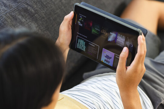 Teenage Asian Boy Browses A Video Streaming Site On A Tablet At Home