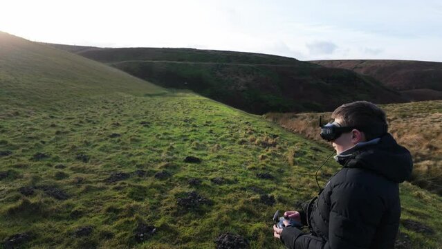 Young boy and his mother outside in the countryside, flying his FPV Drone with a vitual reality headset and practicing his skills sport.