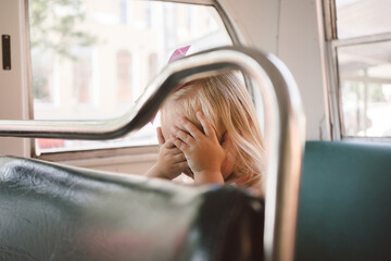 Young girl covers face with hands while sitting on bus seat