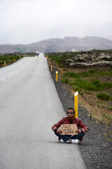 Young man hitch-hiking with cardboard with text