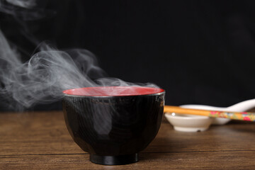 Smoke vape fog rising flowing out of miso soup black red white bowl on dark black background - 736742500