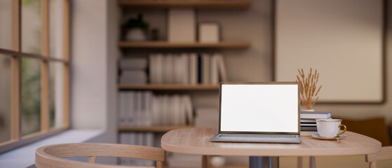 A laptop mockup on a wooden table in a cosy, Scandinavian cafe seating area or a living room.