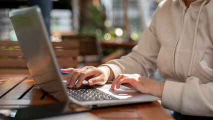 A woman working remotely at a cafe, online on her laptop computer, and typing on the keyboard.