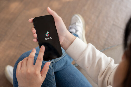 A close-up shot of a woman using the TikTok application on her iPhone while sitting outdoor.