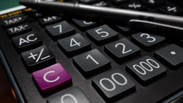 A closeup clip of a larg size buttons calculator with a pen, rotating on an automatic display stand.