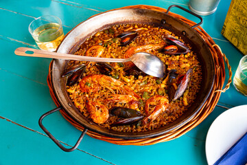 Traditional seafood paella with mussels, calamari and shrimps in frying pan on bright wooden table