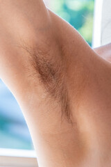 Closeup of long dark hair growing under arm of young female. Concept of hygiene, natural beauty, feminity and body hair growth