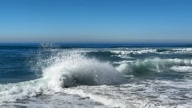 Ocean waves crashing and spraying high together during King tide over blue ocean and blue sky.