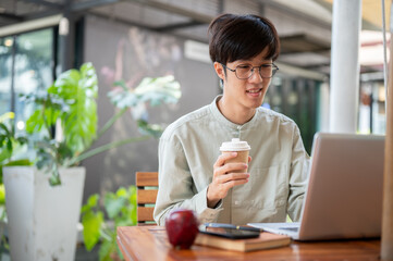 A happy man is sipping coffee and focusing on his work on a laptop, working remotely at a cafe.