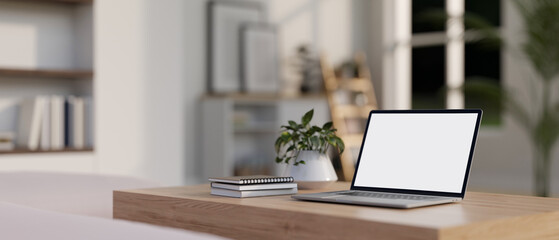 A white-screen laptop computer mockup on a wooden table in a modern white living room.