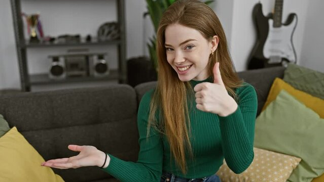 Cheerful, confident young blonde woman presenting ok sign with palm, wearing homely sweater, standing indoors, smiling with thumbs up gesture in a cozy living room, oozing happiness and positivity!