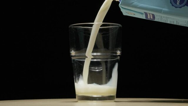 Milk being poured into a clear glass, creating a splash, against a dark background