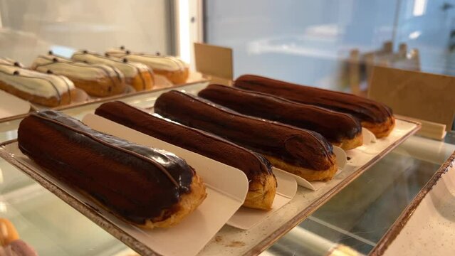 Bunch of ecler pastry covered with chocolate stacked on top of each other at the food market . Counter full of delicious buns and pastries in shop, bakery