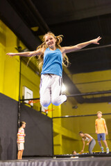 Full length of cheerful teenage girl in sportswear having fun while jumping high on colorful trampoline at game club
