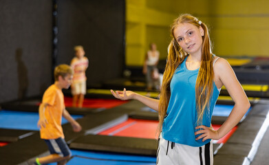 Happy teen girl in blue jersey posing on trampolines during active weekend free time in entertainment center