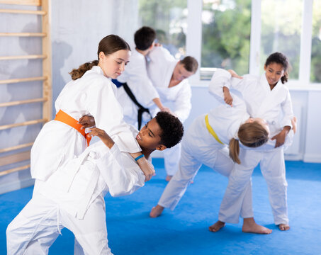 Boy and girl in kimono practicing judo techniques in group at gym..