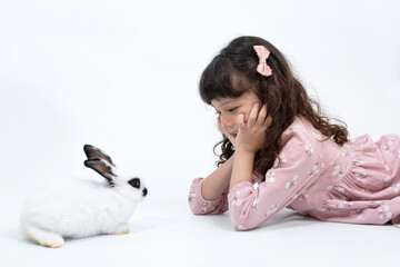 Cute little girl lies on the floor with pet white rabbit on white background, Easter symbol concept