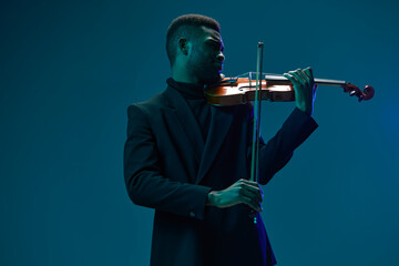 Elegant musician playing the violin in a black suit on a vibrant blue background