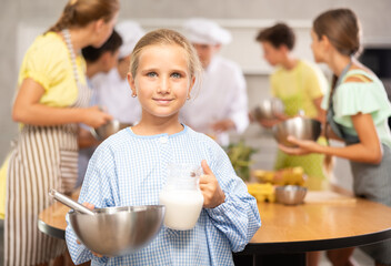 Positive interested tween girl attending group culinary classes for children, standing by table...