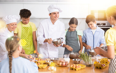 ..Young guy and adult woman chef at master class teaches group of children how to cook food