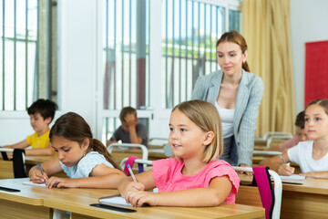 Fototapeta premium Pupils sitting in classroom during lesson. Female teacher standing behind.