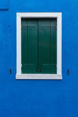 Front view of a Venetian building facade windows with wooden shutters and painted walls.