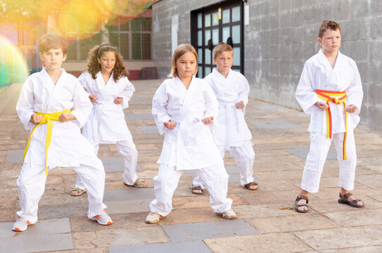 Kids in kimono doing kata moves on street during outdoor karate training.