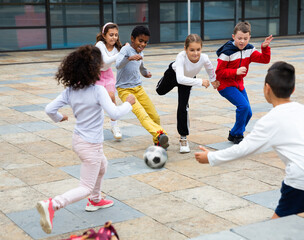 Happy tween girls and boys of different nationalities playing football in schoolyard during break...