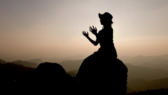 Slow motion, Silhouette of woman praying over beautiful sunrise background, beautiful landscape, pay homage, spirituality and religion, Christianity concept.
