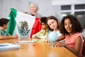 Concentrated ten-year-old schoolgirl is studying the history of Mexico in lesson and is looking for on her on the globe - obrazy, fototapety, plakaty