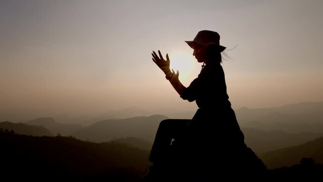 Slow motion, Silhouette of woman praying over beautiful sunrise background, beautiful landscape, pay homage, spirituality and religion, Christianity concept.