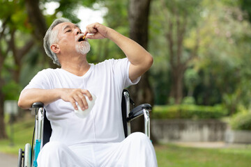 senior man sitting on wheelchair and taking medicine in the park