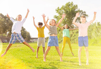 Fototapeta premium Group of children, boys and girls, jumping together on green grass in a park on sunny day