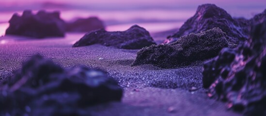 A cluster of rocks resting on a sandy beach with purple hues, surrounded by water. The natural...