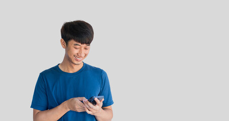 A young Asian man in his 20s wearing a blue t-shirt is happily playing on a mobile phone isolated...
