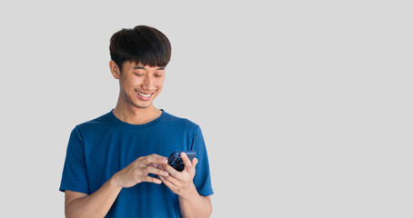 A young Asian man in his 20s wearing a blue t-shirt is happily playing on a mobile phone isolated on a white background. Typing and chatting with friends via smartphone. Online social concept.