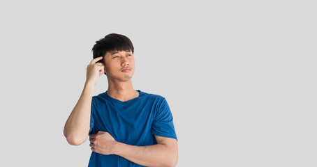 A young Asian man in his 20s wearing a blue t-shirt is looking suspicious and has a confused expression or is thinking, isolated on a gray background.