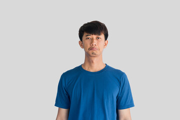 A young Asian man in his 20s wearing blue t-shirt is depressed and worried in distress standing on a gray background. Crying in anger and fear. Sad expression concept.
