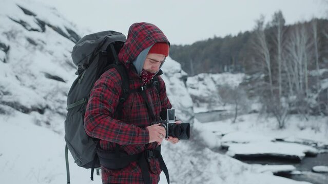Professional photographer standing on snow-covered mountain, setting camera and taking pictures of scenic nature during winter hiking trip