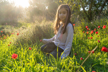 Serene Child Sits In A Field Of Blooming Red Anemones, With The Setting Sun Behind Her.
