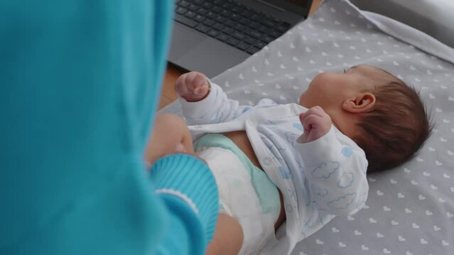 Over shoulder of unrecognizable mother changing diaper of her little baby son on table at homeOver shoulder of unrecognizable mother changing diaper of her little baby son on table at home