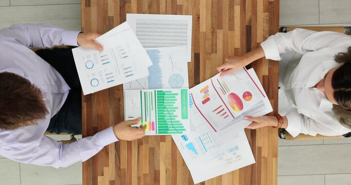 Colleagues put paper sheets with data on table in office