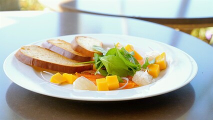 Gourmet tropical fruit salad with fresh salmon and mixed greens accompanied by artisan bread slices. Modern culinary presentation and healthy dining options.