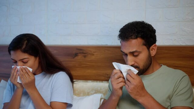 Indian sick couple sneezing due to suffering from cold or flu virus while sleeping at bedroom - concept of infection, relationship support and influenza