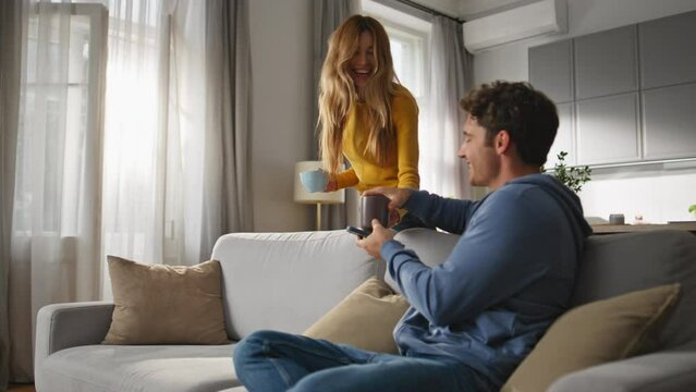 Smiling man browsing smartphone chilling sofa closeup. Happy wife bringing tea