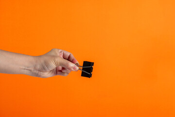 Hand and black paperclip on orange background.