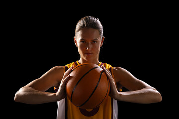 Young Caucasian female basketball player poses confidently in basketball attire on a black backgroun