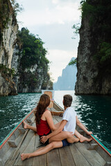 A couple of young people in love are sailing on a boat and sitting on the stern, admiring the scenery around, rear view.