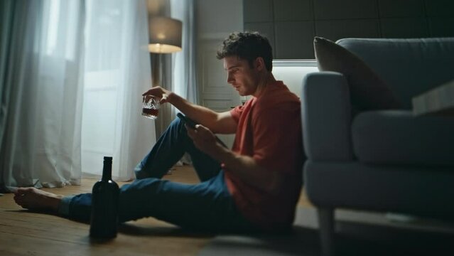 Relaxed man drinking cognac in night home interior. Laughing guy check sms alone