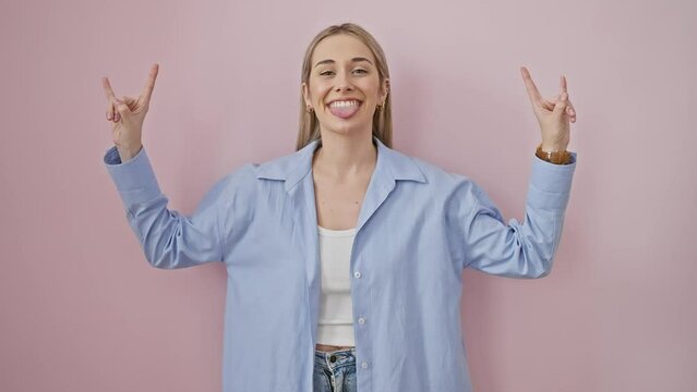 Wild young blonde starlet rocking out, hands forming heavy metal symbol, displaying crazy passion for music over pink isolated background